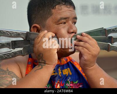 Thai Chinese Taoist devotee (mah song, masong) pierces his right cheek with six knives during the Phuket Vegetarian Festival. Stock Photo