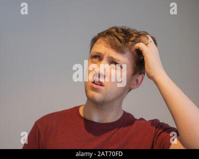 A young man looking very confused and scratching his head Stock Photo