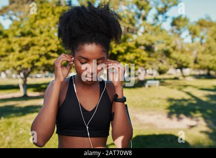 Close-up of an athletic young african american woman inserting earphones in her ears listening to music in the park before doing some fitness Stock Photo