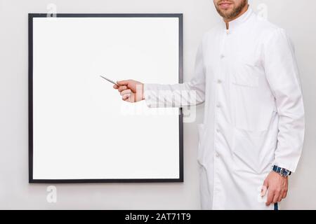 Man in white uniform pointing on a picture frame or poster for mock up. Doctor or chef showing empty frame, medicine, business and advertisement Stock Photo