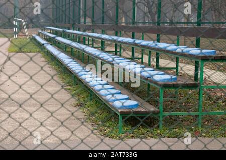 Grand stand bleachers with plastic blue seats in small stadium, behind the wire fence Stock Photo