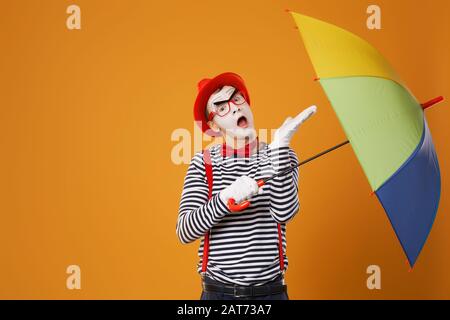 One mime with multi-colored umbrella on empty orange background in studio Stock Photo