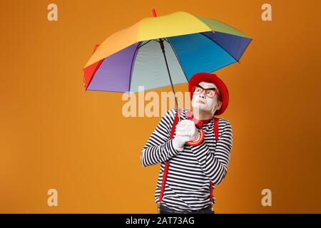 Mime with multi-colored umbrella on empty orange background in studio Stock Photo