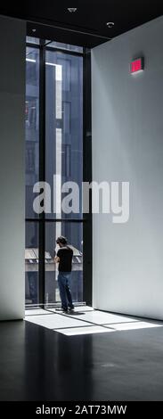 June 2019. Lonely sad man looking down through a big vertical window in the Museum of Modern Art (MOMA) in New York City, United States. Red exit sign Stock Photo