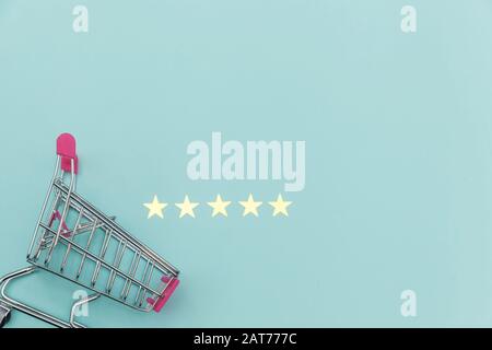 Small supermarket grocery push cart for shopping toy with wheels and 5 stars rating isolated on pastel blue background. Retail consumer buying online assessment and review concept Stock Photo