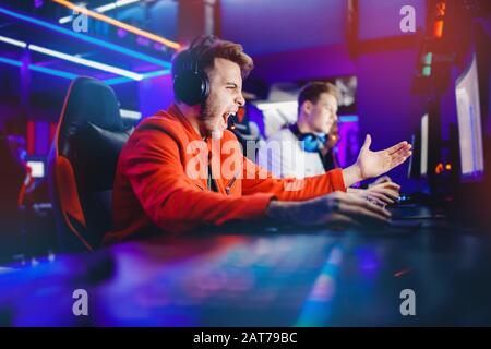 Streamer young man rejoices in victory professional gamer playing online games computer with headphones, neon color Stock Photo