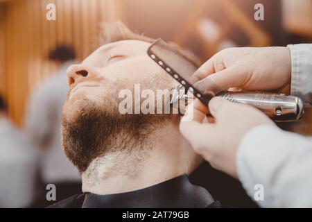 Hipster client man visiting in barber shop shaving beard, Vintage tinted brown Stock Photo