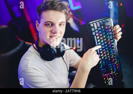 Professional young man player in online video game esport advertises headphones, keyboard and mouse for computer, blurred background Stock Photo