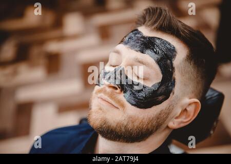 Spa facial skin care for men, applying removal of black charcoal mask from nose face in barbershop Stock Photo