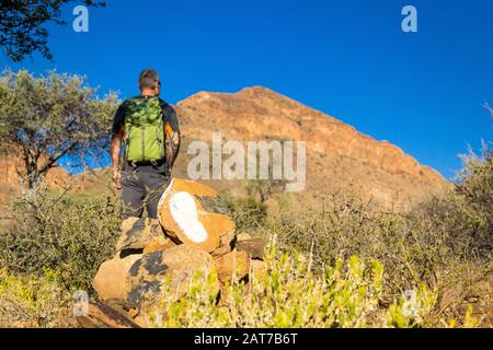 Footprint on a stone, that is signposting the Olive Trail of Namib Naukluft Park; in the background a hiker looking to a mountain, Namibia, Africa Stock Photo