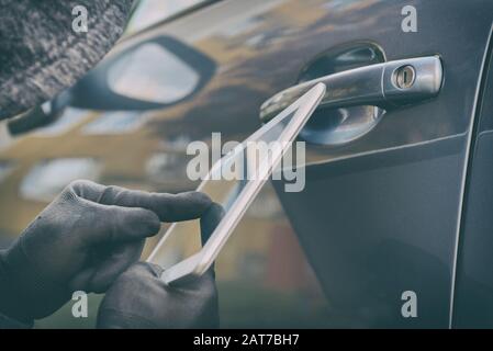 Hooded thief tries to break the car's security systems with tablet. Hacking modern car concept Stock Photo