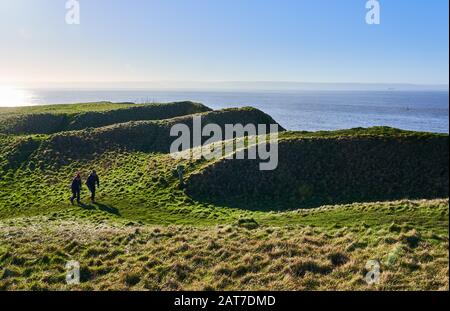 Walkers on the Wales Coast Path passing the earthworks of Nash Point Iron Age Hill Fort on the Glamorgan coast of South Wales Stock Photo