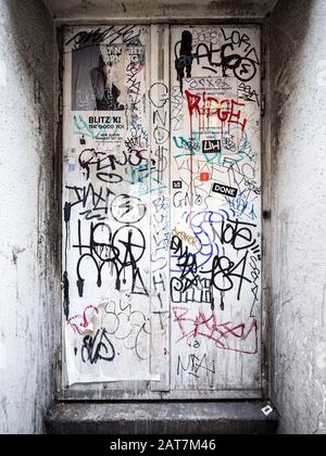 Urban Anarchy. Detail of a recessed white door covered in graffiti tags defying a defaced warning sign. Stock Photo