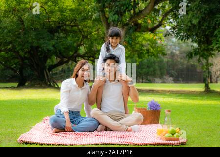 Asian teen family happy holiday picnic moment in the park with father, mother and daughter looking at camera and smile to happy spend vacation time to Stock Photo