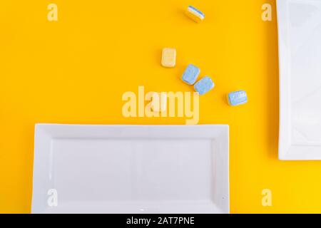 Cleaning dishwasher tablets with white plate on a yellow background. Group of bright colored soap tablet for washing dishes. Cleaning equipment - dete Stock Photo
