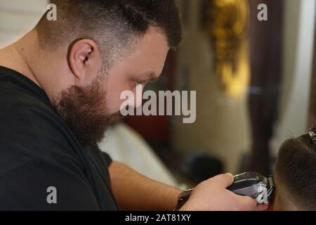 Barber cuts hair of men in the barbershop using hair clipper, hairdresser makes hairstyle Stock Photo