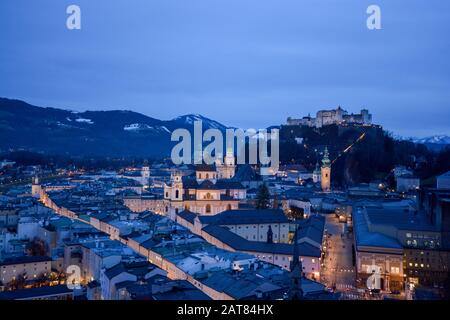 Salzburg evening cityscape with main Cathedral, Kollegienkirche and illuminated streets of old town on background of mountains in clouds Stock Photo