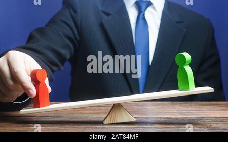 Man opposes green figure to red opponent on scales. Give an advantage, change balance of power, change outcome of confrontation. Invisible helping han Stock Photo