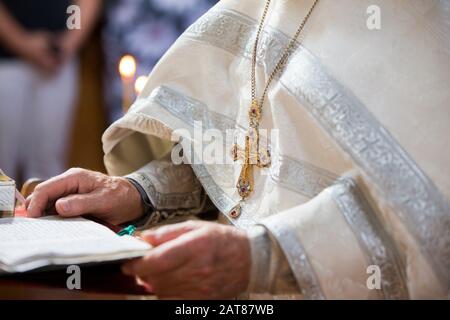 Orthodox religion. Hands of the priest against the background of the cross and candles. Stock Photo