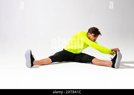 doing stretching first. young man in sportwear training and stretching his muscle on white background Stock Photo