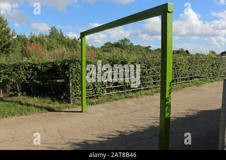 Country park green painted metal car park height restriction barrier, with a metal fence and hedge with blue sky and white cloud. Stock Photo