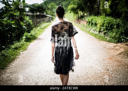 Rear view of woman wearing black lace dress walking down a rural country road. Stock Photo