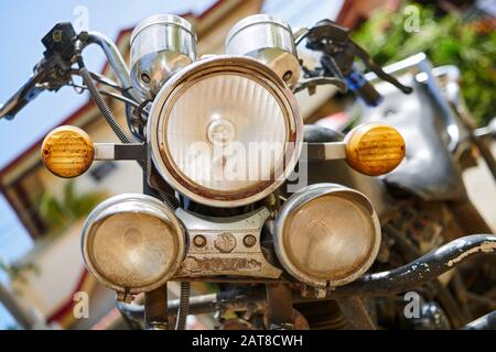 A close-up low angle view of the front head lights of an old, dirty and rusty motorcycle parked in a small town in the Philippines Stock Photo