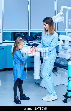 Pediatric dentist showing basic dental hygiene principles. Female pediatric dentist showing a treatment for adorable little girl in a hospital Stock Photo