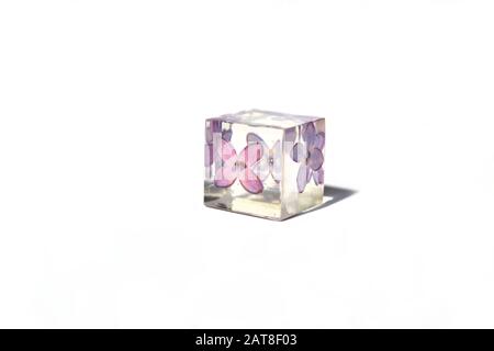Beautiful simple violet and white background suitable for text input. Handmade epoxy resin cube with lilac flower, isolated on white background. Stock Photo