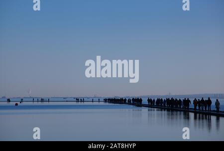 People walking around the Marine Lake at West Kirby on the Wirral Peninsula in winter on the wall path between the boating lake and the Dee estuary Stock Photo