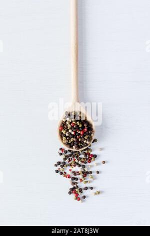 Multi colorful pepper seeds on wooden spoon on white wooden background. Photo of horizontal orientation. Stock Photo