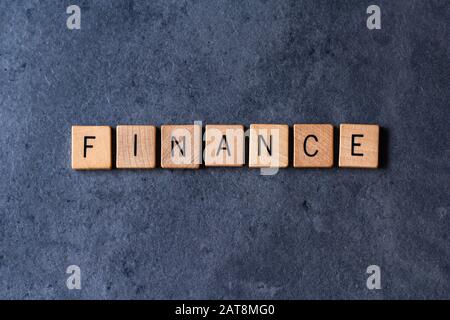 'Finance' spelled out in wooden letter tiles on a dark rough background Stock Photo