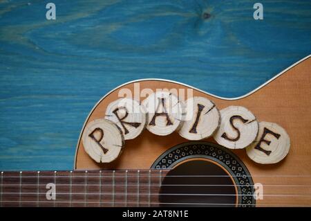 guitar on teal wooden background with wood pieces on it lettering the word: PRAISE Stock Photo