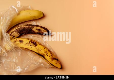 spoiled three bananas lie in a plastic bag on the table. Fruit concept in plastic. Life without waste and without plastic. Save the environment. Stock Photo
