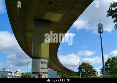 low anglel view of concrete overpass highway underside and heavy support pier. street lights and blue sky with white clouds. curving high speed road Stock Photo