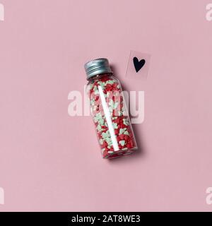A bottle filled with heart shaped candies and love symbol on pink background. Love or Valentine's Day concept. Stock Photo