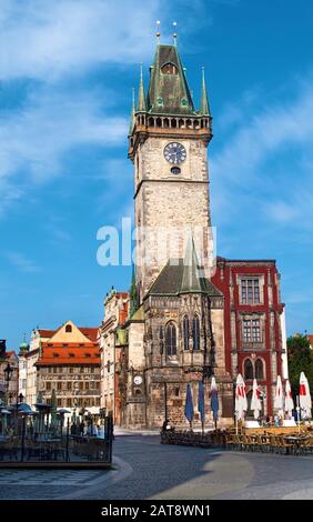 View of the street near Old Town Hall with its high clocktower and red tiled roof against vibrant blue sky and white couds in the morning. Prague, Che Stock Photo