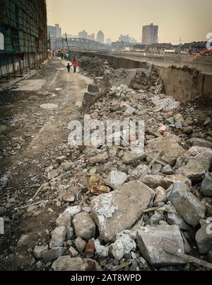 Rubble in front of construction site covered by scaffolding, woman with child walking in background. Stock Photo
