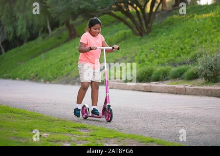 A young girl riding a pink scooter in a narrow street. Stock Photo