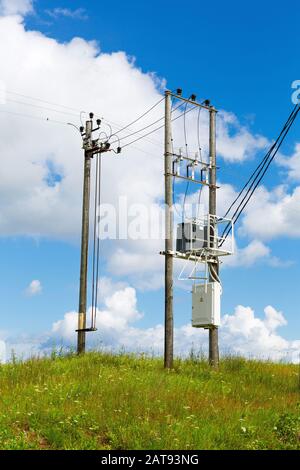 Transformers of an electrical post with power lines cables against bright blue sky. Transformer with the electricity poles in the field. Stock Photo