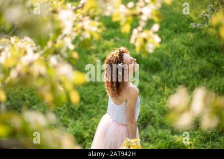 Young attractive girl walks in spring green park enjoying flowering nature. Healthy smiling girl spinning on the spring lawn. Allergy without. Stock Photo