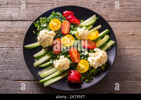Flat lay Salad of fresh vegetables on black plate over wooden background, close up Stock Photo