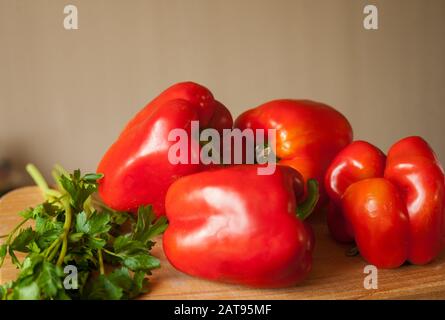 red ripe eco-friendly peppers with sprigs of green dill and parsley lie on a wooden board Stock Photo