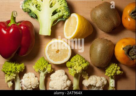 vegetables and fruits on a wooden board composition: persimmons, kiwi, lemon, romanesco, broccoli, cauliflower, bell pepper Stock Photo