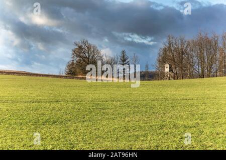 Hunting watchtower at the edge of the field. Dramatic sky. Hunting evening. Agricultural landscape in the Czech Republic. Hunting observatory. Stock Photo