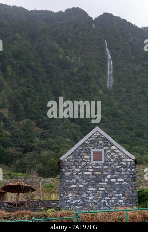 Waterfall on a mountain of Madeira with a stone house on the foreground, in Madeira, Portugal Stock Photo