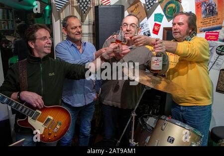 31 January 2020, Schleswig-Holstein, Klein Pampau: Iain Macnab (2nd from right), former mayor of the small community of Brunsmark near Mölln, toasts with his fellow musicians Sigi Krei (l), Peter Kruschel (2nd from left) and Wolle Flensky (r) with a whisky during the rehearsal of the band 'Lucky Devils'. The Scot Macnab has lived in Germany for over forty years and has been mayor of the town of 160 inhabitants for eleven years. With the brexite Macnab has to resign from his office as mayor and is also no longer allowed to participate in the municipal council. Photo: Jens Büttner/dpa-Zentralbil Stock Photo