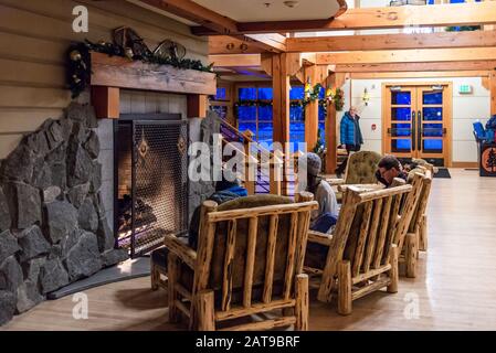 Family gathers in front of the fireplace in the lobby of the Old Faithful Snow Lodge. Yellowstone National Park, Wyoming, USA Stock Photo