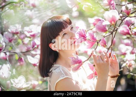 woman holds branch of magnolia with pink flowers. Allergy to flowering in spring. Risk of swelling of quintessential. Stock Photo