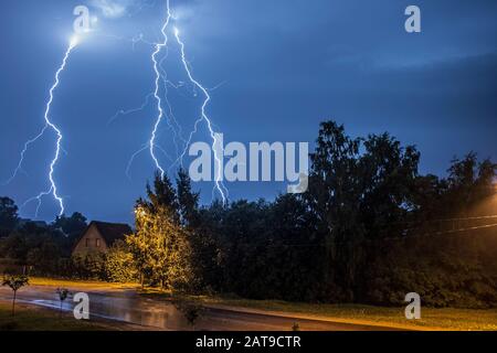 Thunder lightning on a summer night over a small village with trees and houses Stock Photo